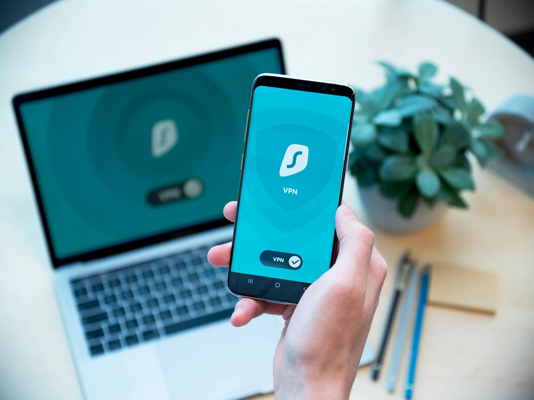 Dłoń trzymająca smartfon z aplikacją VPN obok otwartego laptopa