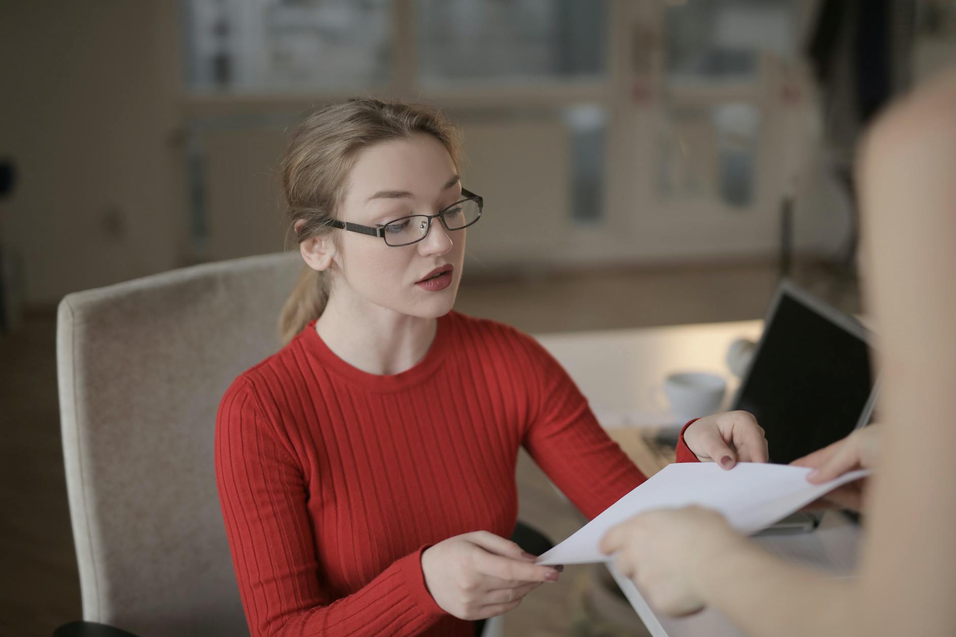 Pracowniczka w czerwonym swetrze odbiera dokument w jasnym biurze