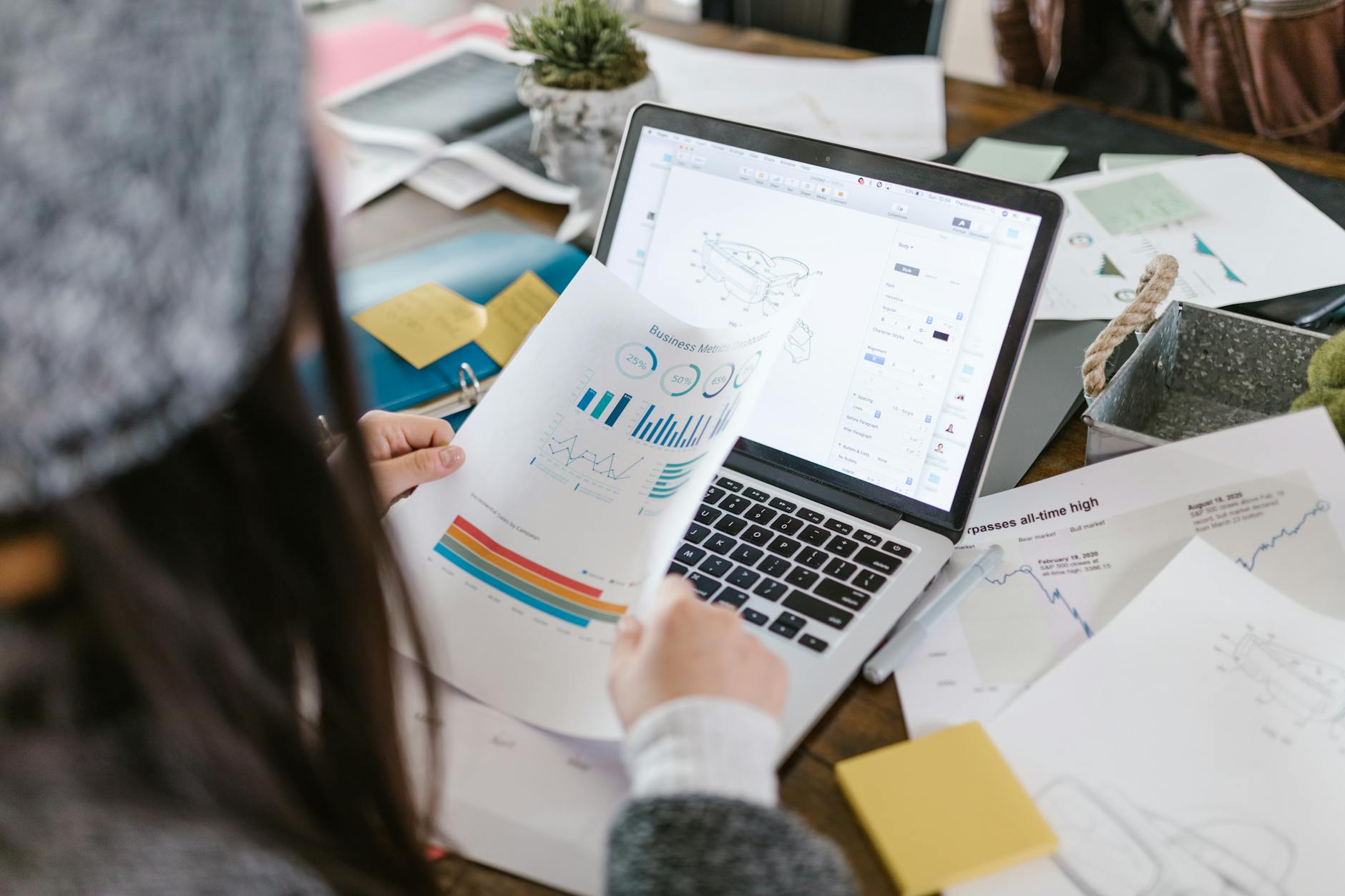 Pracownik analizuje wydrukowane wykresy przy laptopie w nowoczesnym biurze