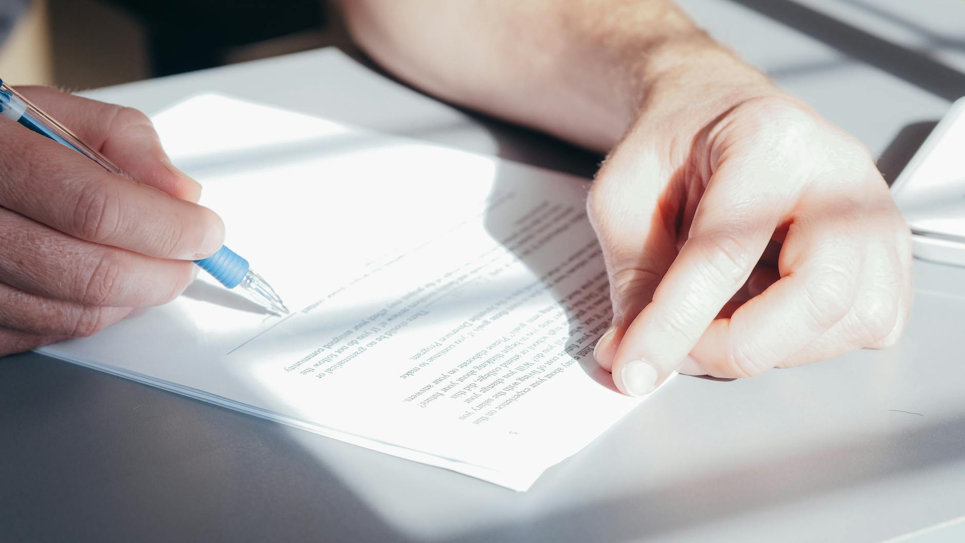 Dłoń podpisująca papierową umowę niebieskim długopisem z bliska