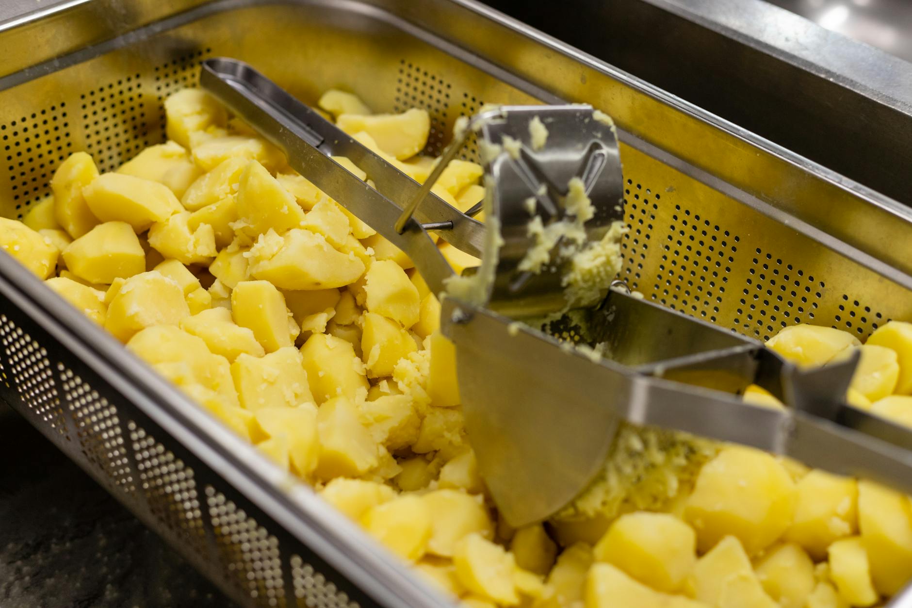 Gorące żółte ziemniaki przeciskane przez praskę w kuchni zawodowej