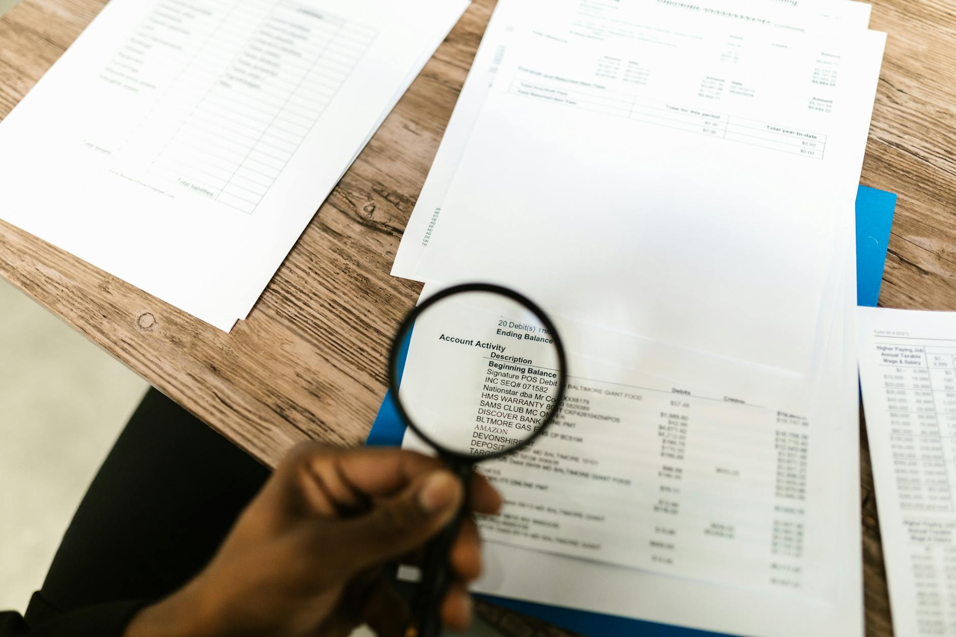 Dłoń z lupą analizuje dokumenty finansowe