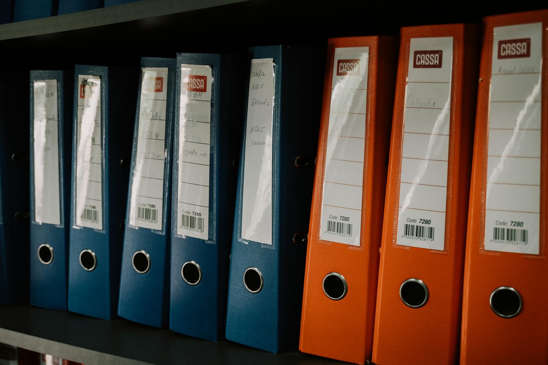 Kolorowe segregatory biurowe ustawione równo na półce w archiwum