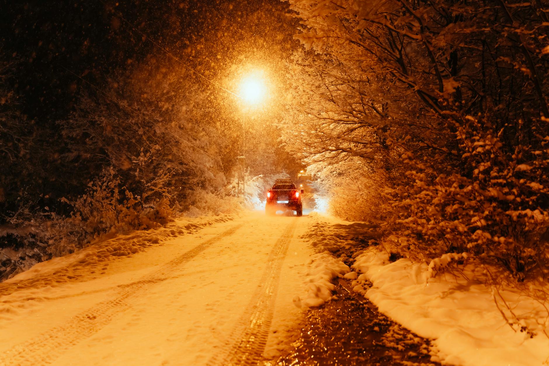 Samochód jedzie nocą po ośnieżonej drodze w świetle latarni