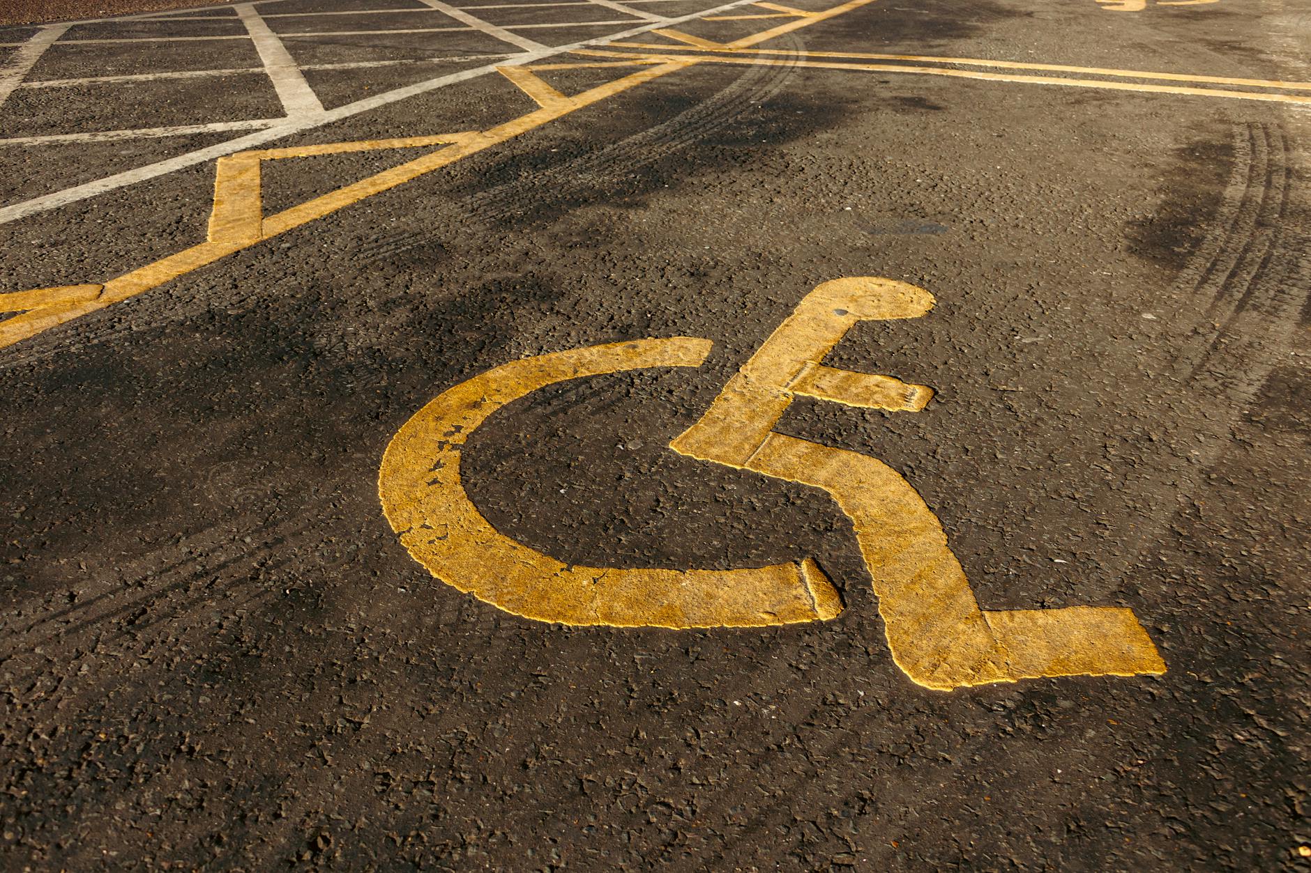 Dostępność cyfrowa w zamówieniach: jak opisać wymagania dla wykonawcy Żółty symbol wózka inwalidzkiego namalowany na asfalcie parkingu